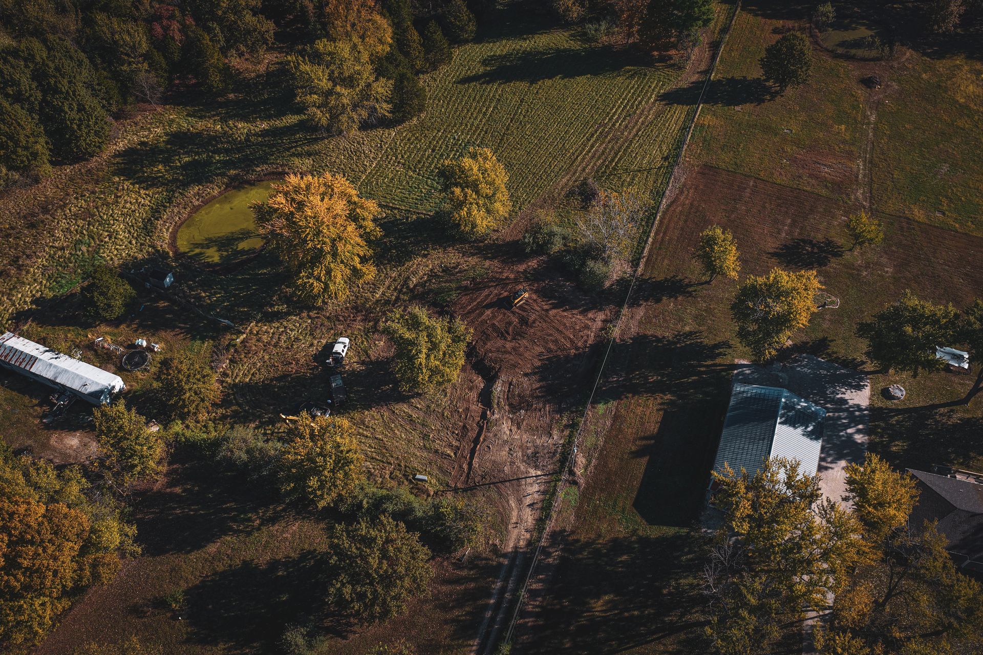 Aerial view of a rural property with a house, outbuildings, and autumn trees in a fenced clearing