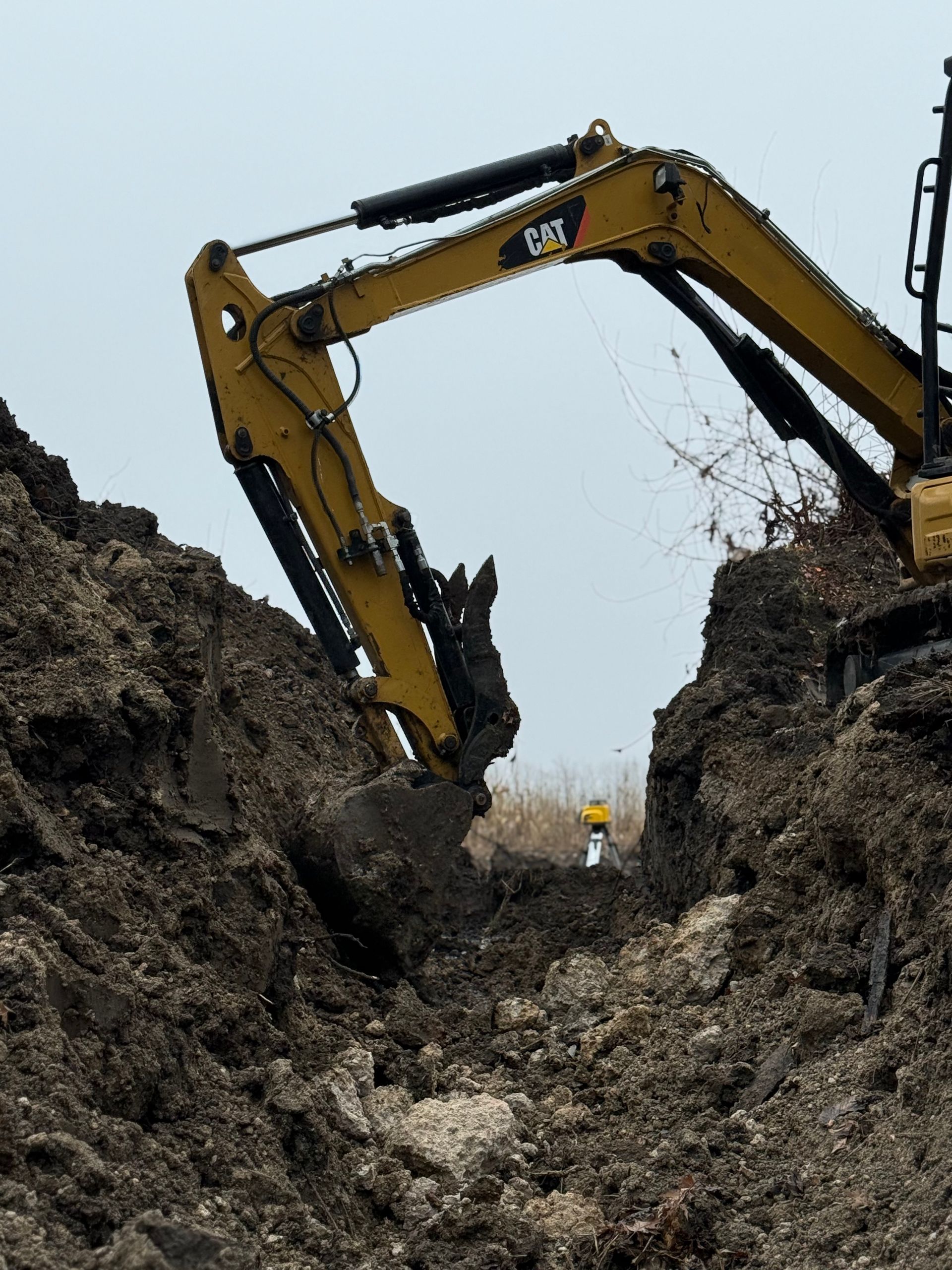 Yellow excavator digging a trench between steep dirt walls