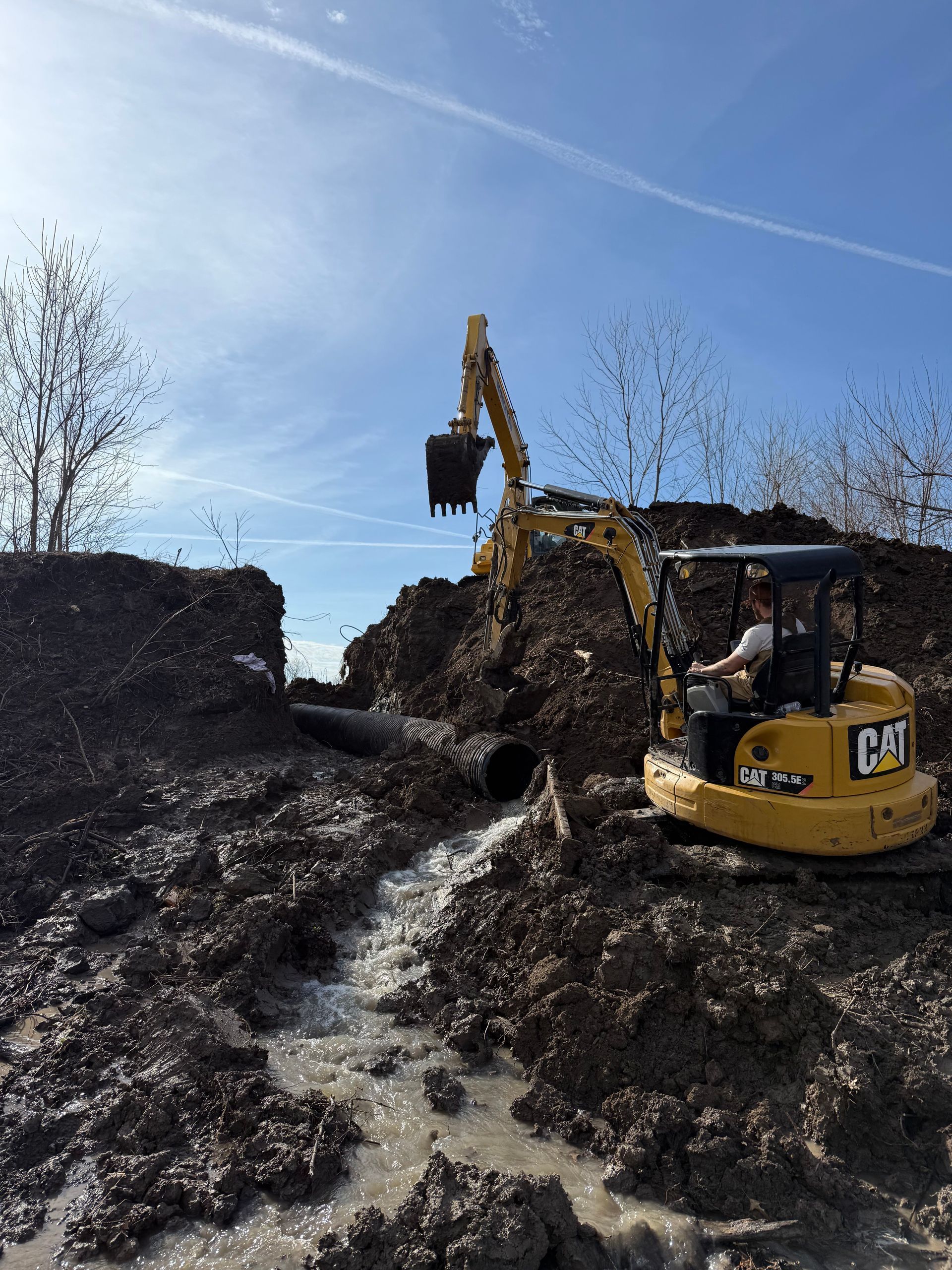 Yellow excavator digging a dirt mound under a clear blue sky