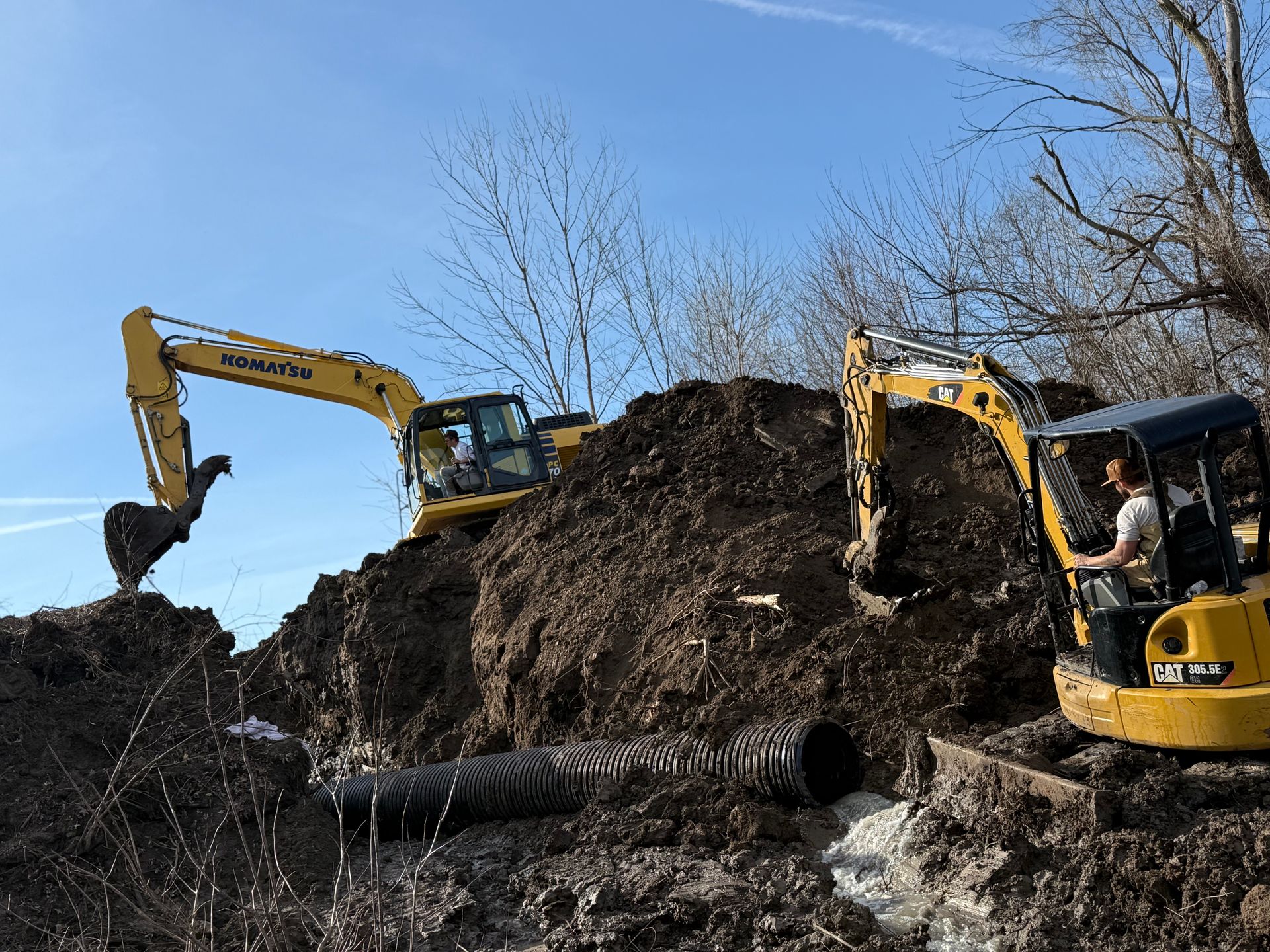 Two yellow excavators digging a large dirt mound under a clear blue sky