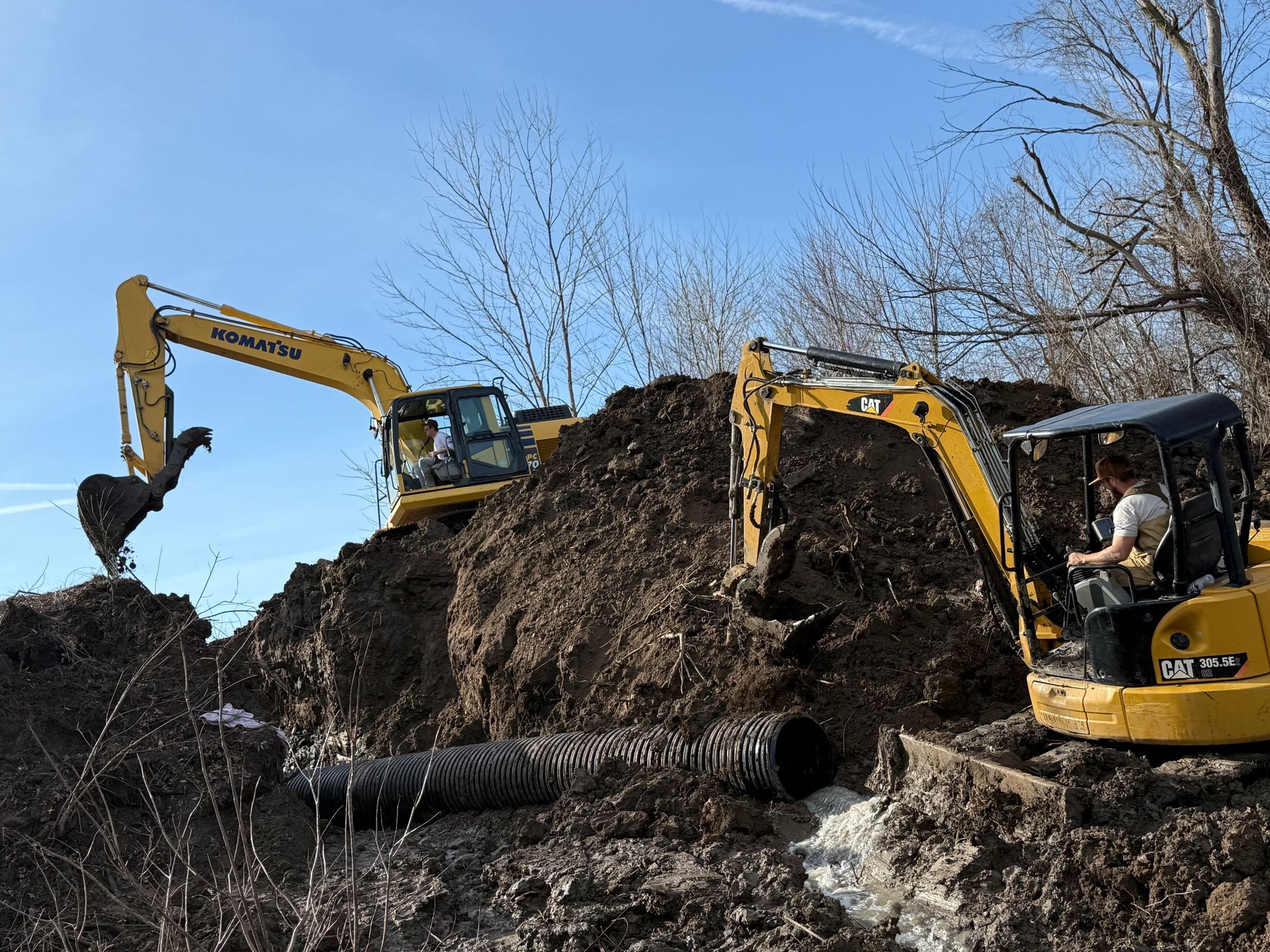 Two yellow excavators digging a large dirt mound under a blue sky