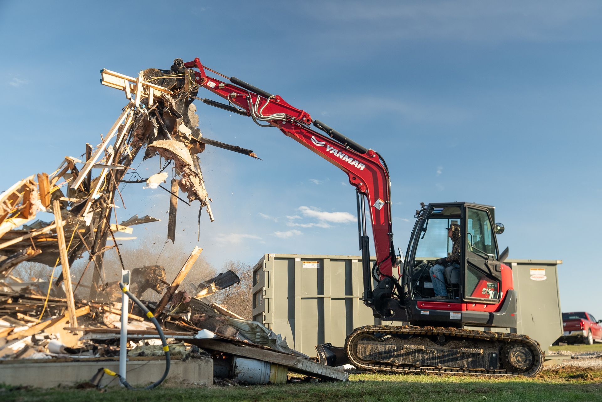Red excavator demolishing a collapsed building under a blue sky