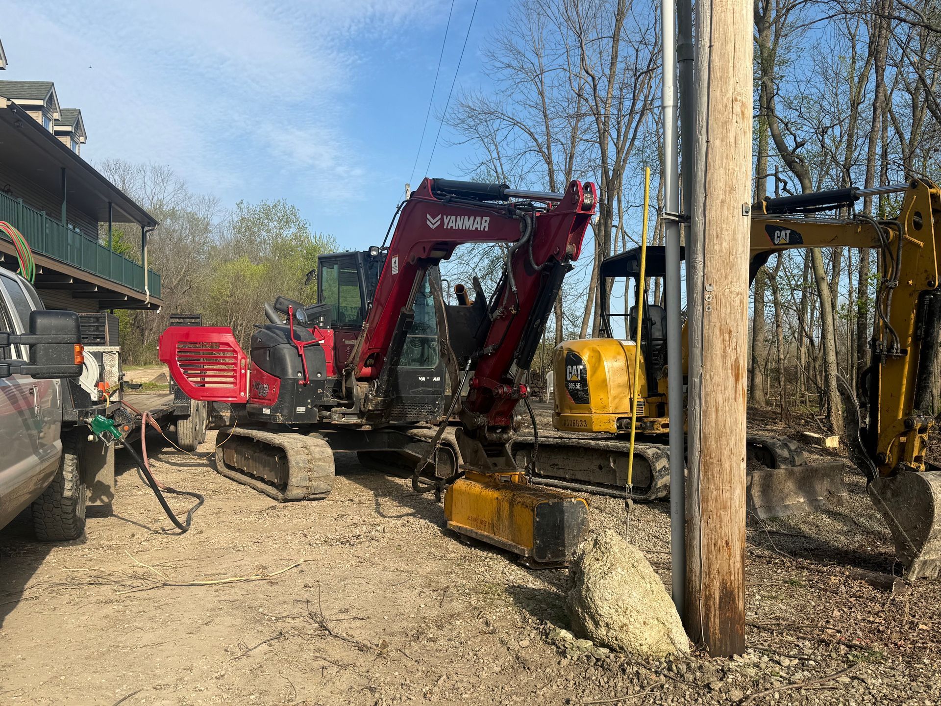 Red excavator beside a building on a muddy construction site with utility poles and equipment