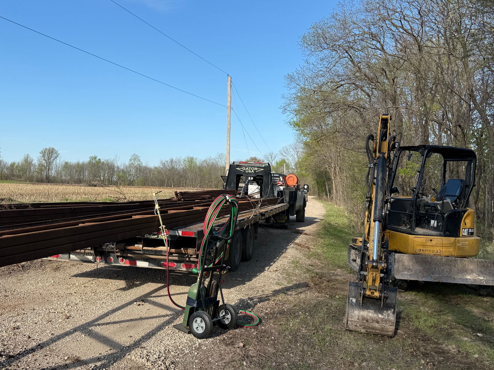 Railroad maintenance equipment parked beside tracks on a sunny rural roadside.