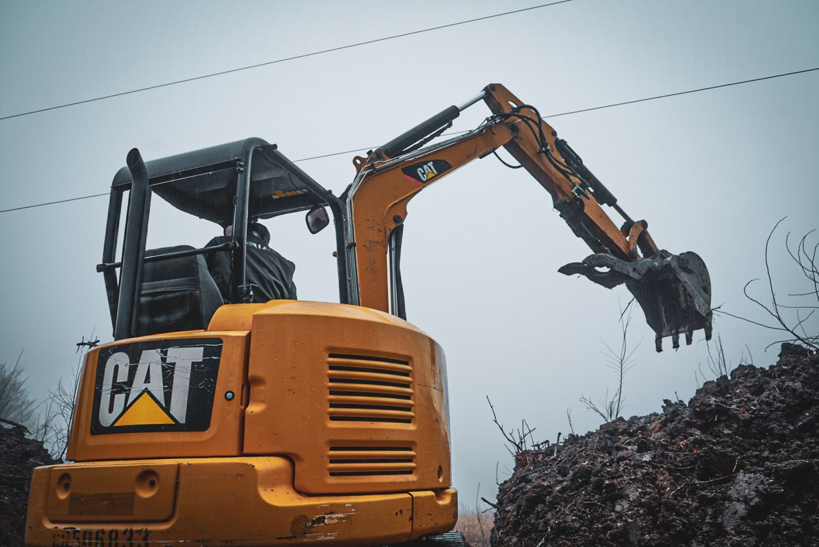 Yellow CAT excavator lifting debris against a gray sky