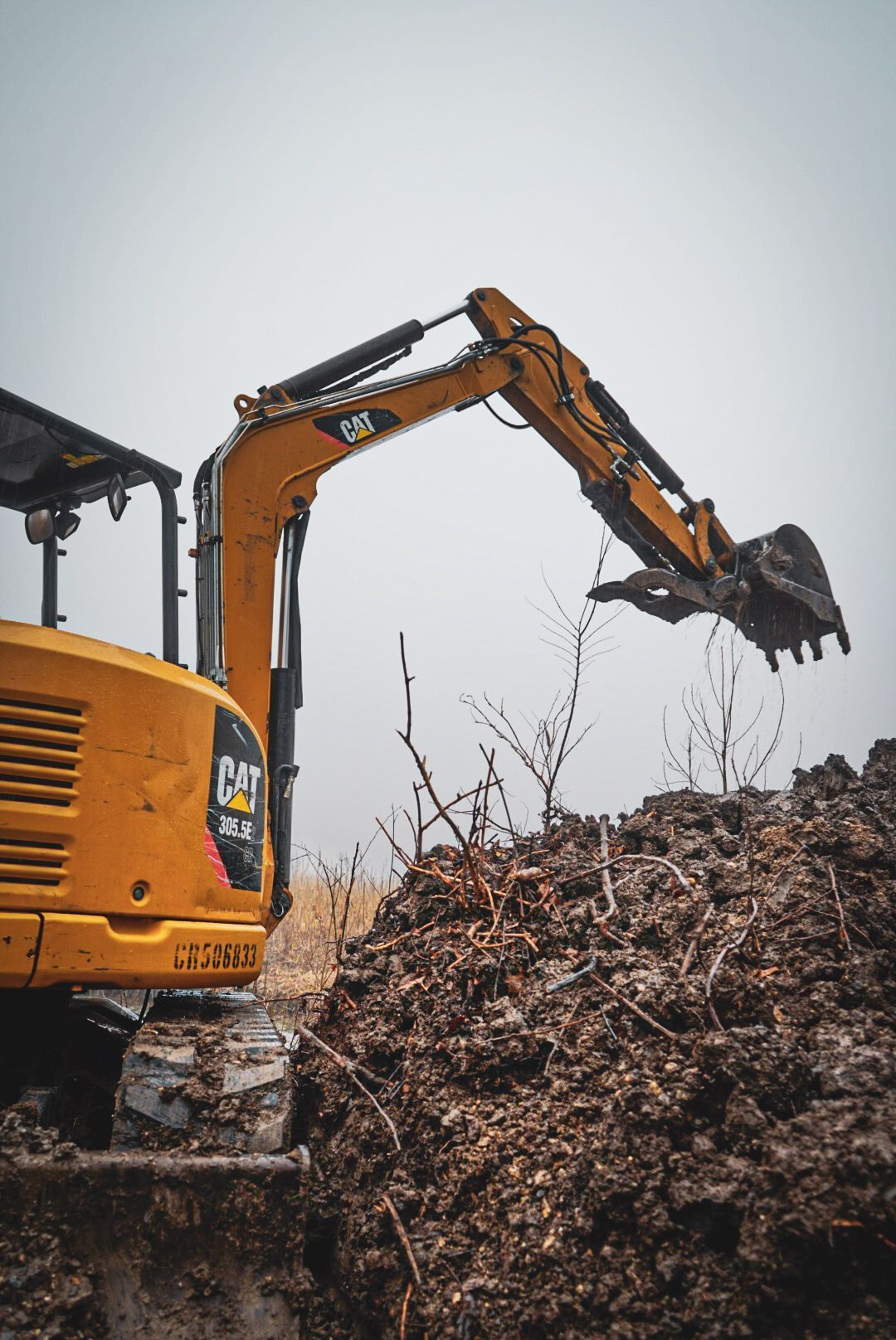 Orange excavator digging a dirt pile with its bucket raised at a landfill