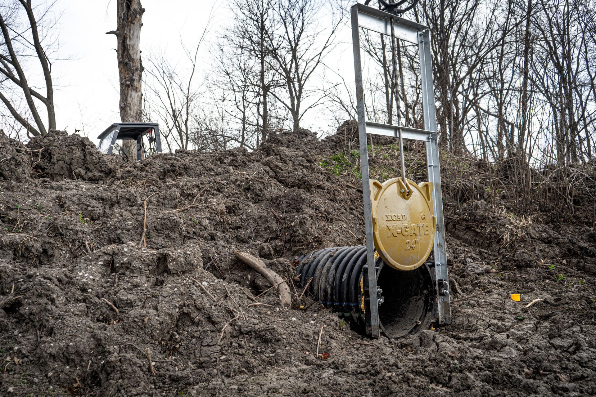Mud-covered yellow door-like panel beside a black pipe in a muddy wooded area