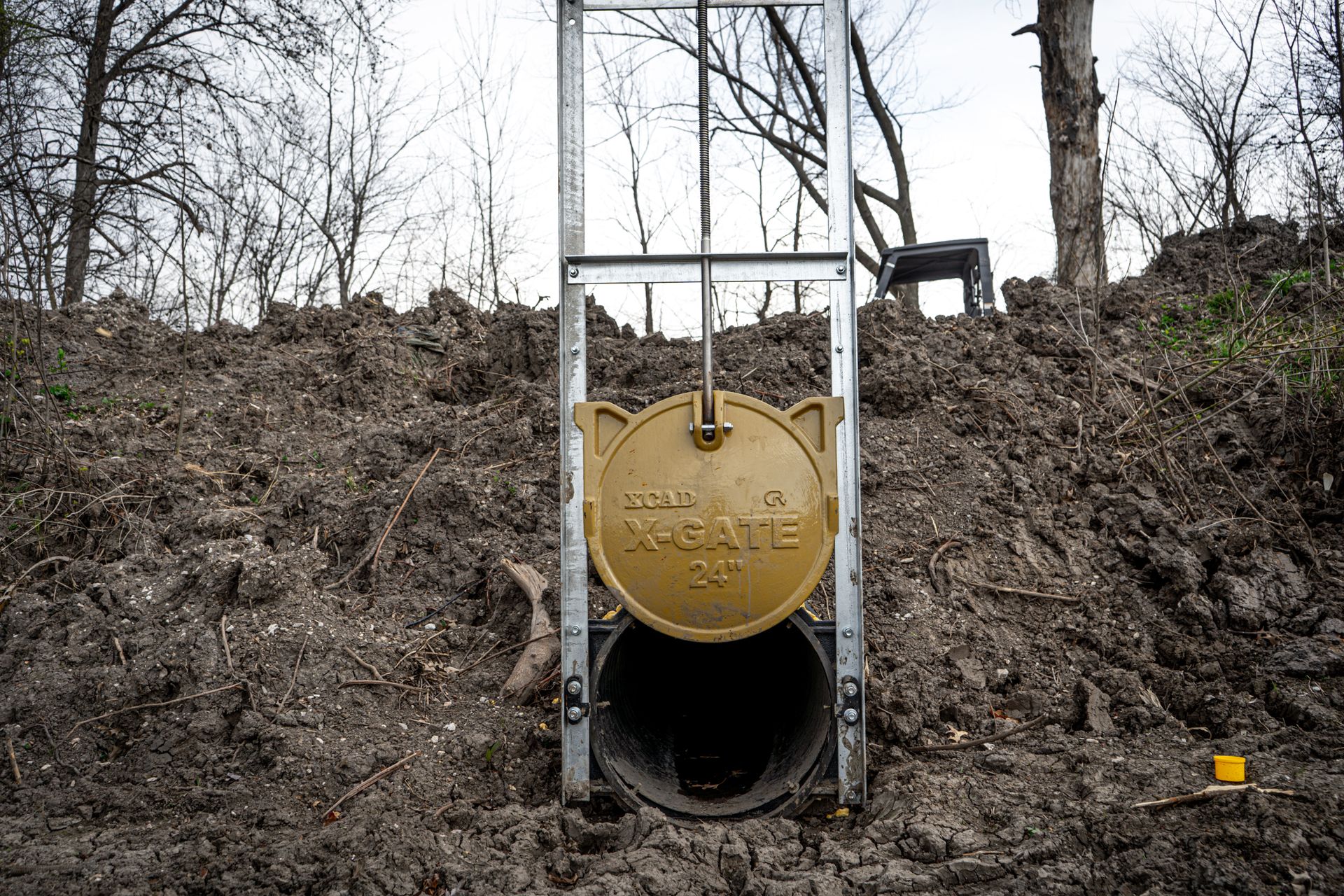 Yellow round hatch on a metal structure embedded in a dirt hillside, with bare trees above.