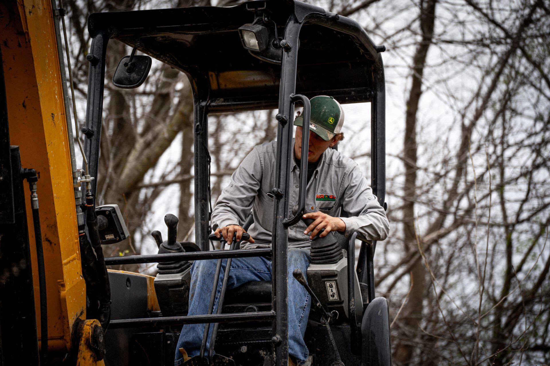 Construction worker operating a yellow excavator in a wintery wooded area