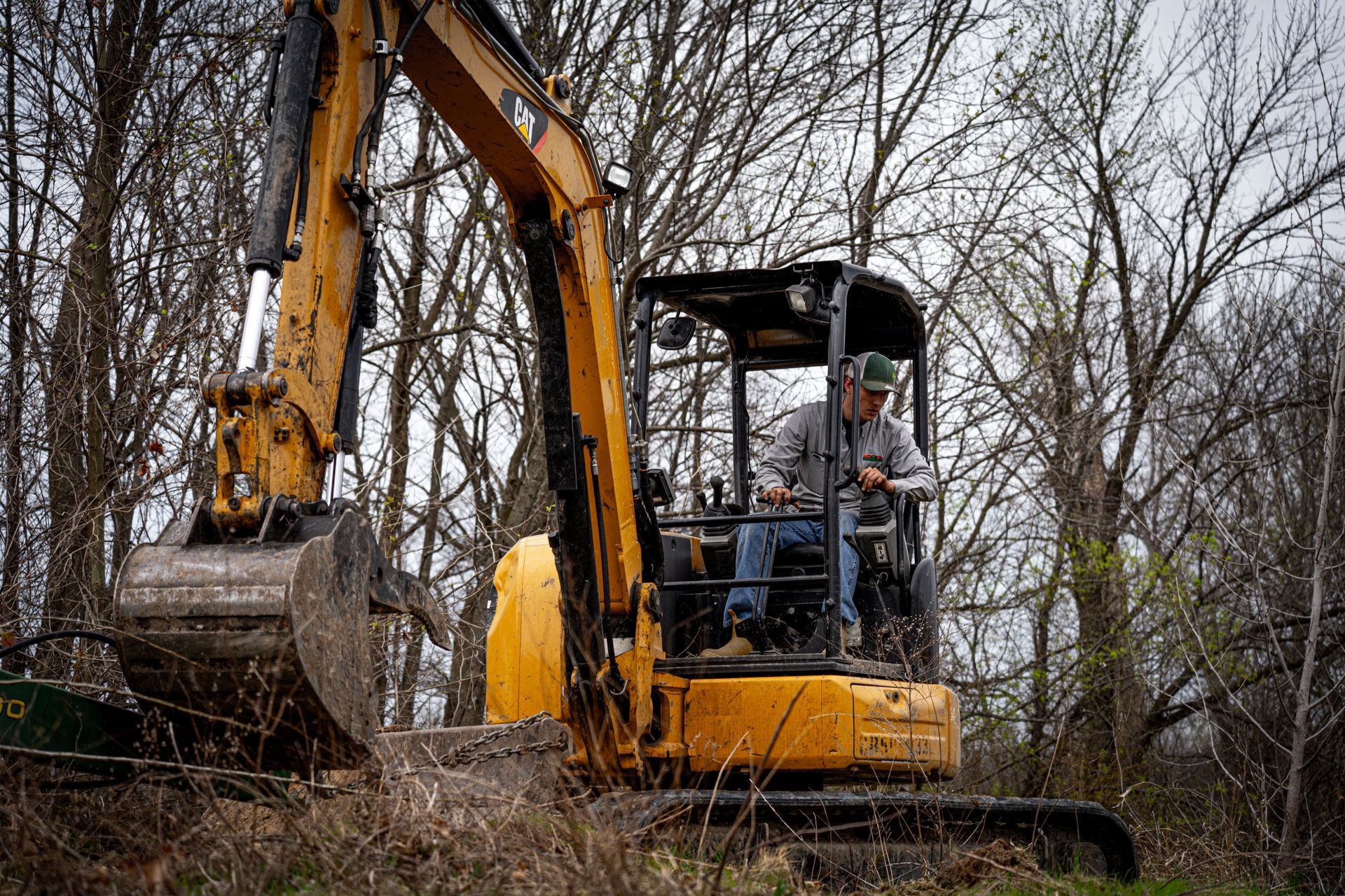 Yellow excavator clearing brush in a wooded area with a person in the cab
