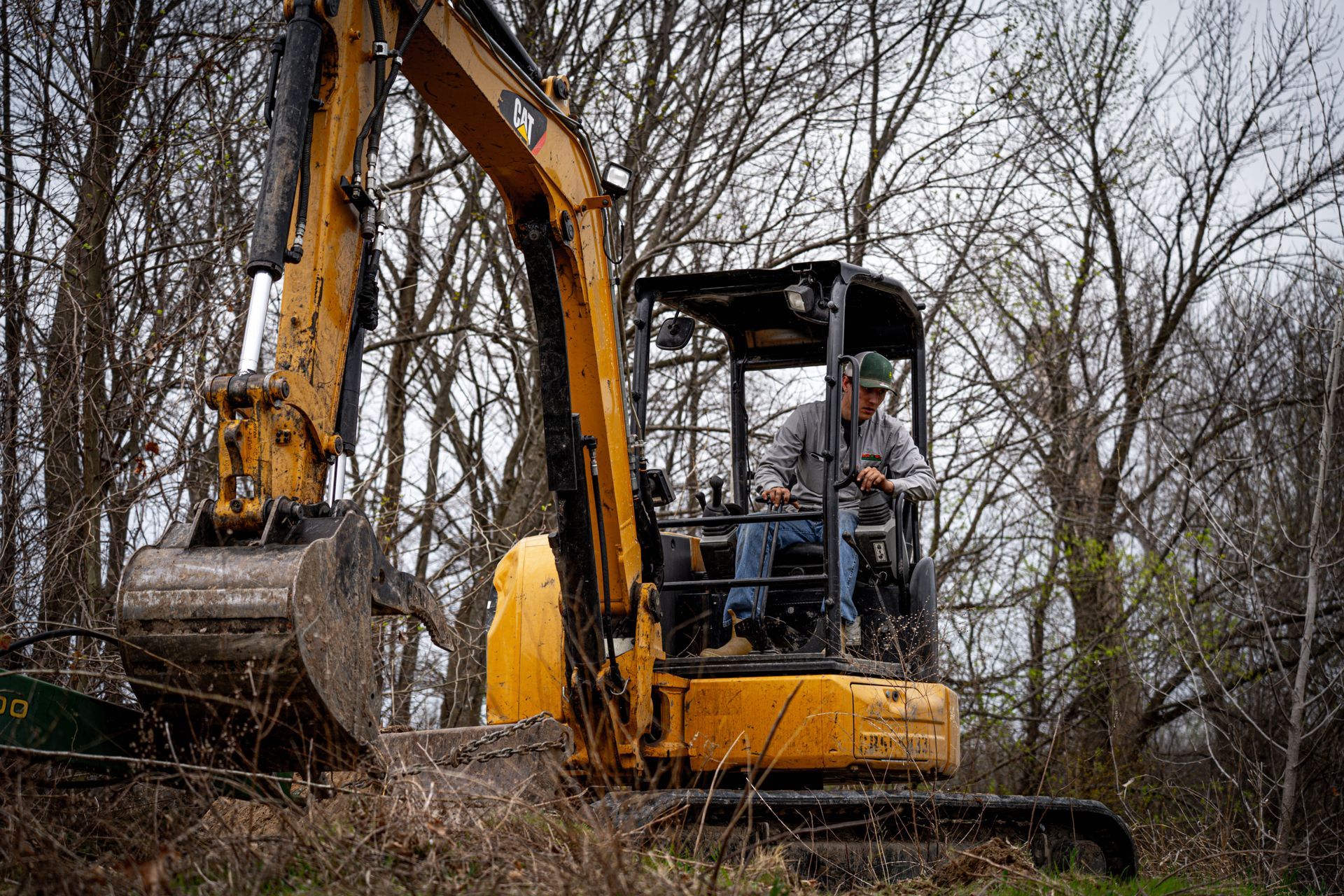 Yellow excavator with operator clearing brush in a wooded area