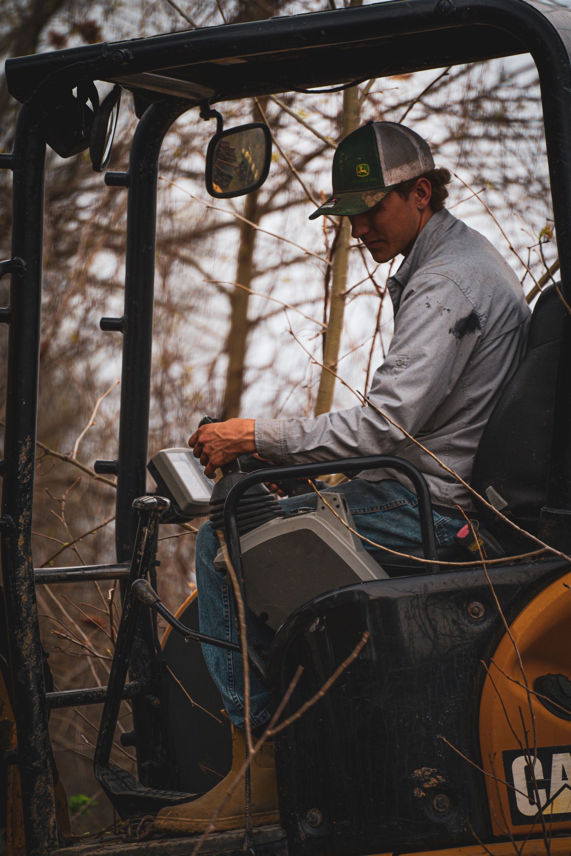 Worker operating a CAT machine inside the cab, wearing a gray shirt and cap.