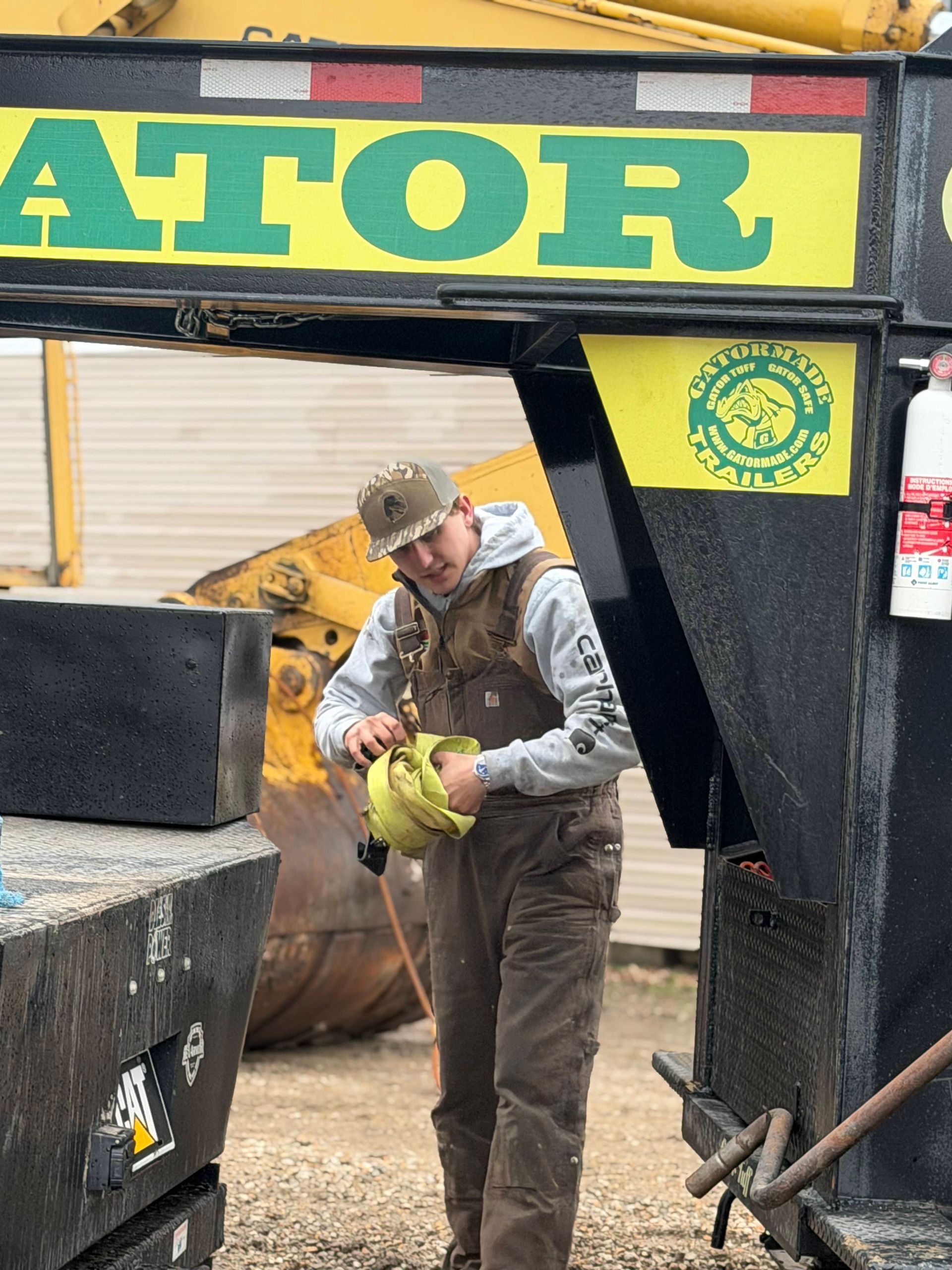 Worker in a black-and-yellow industrial setting inspecting a yellow object near machinery