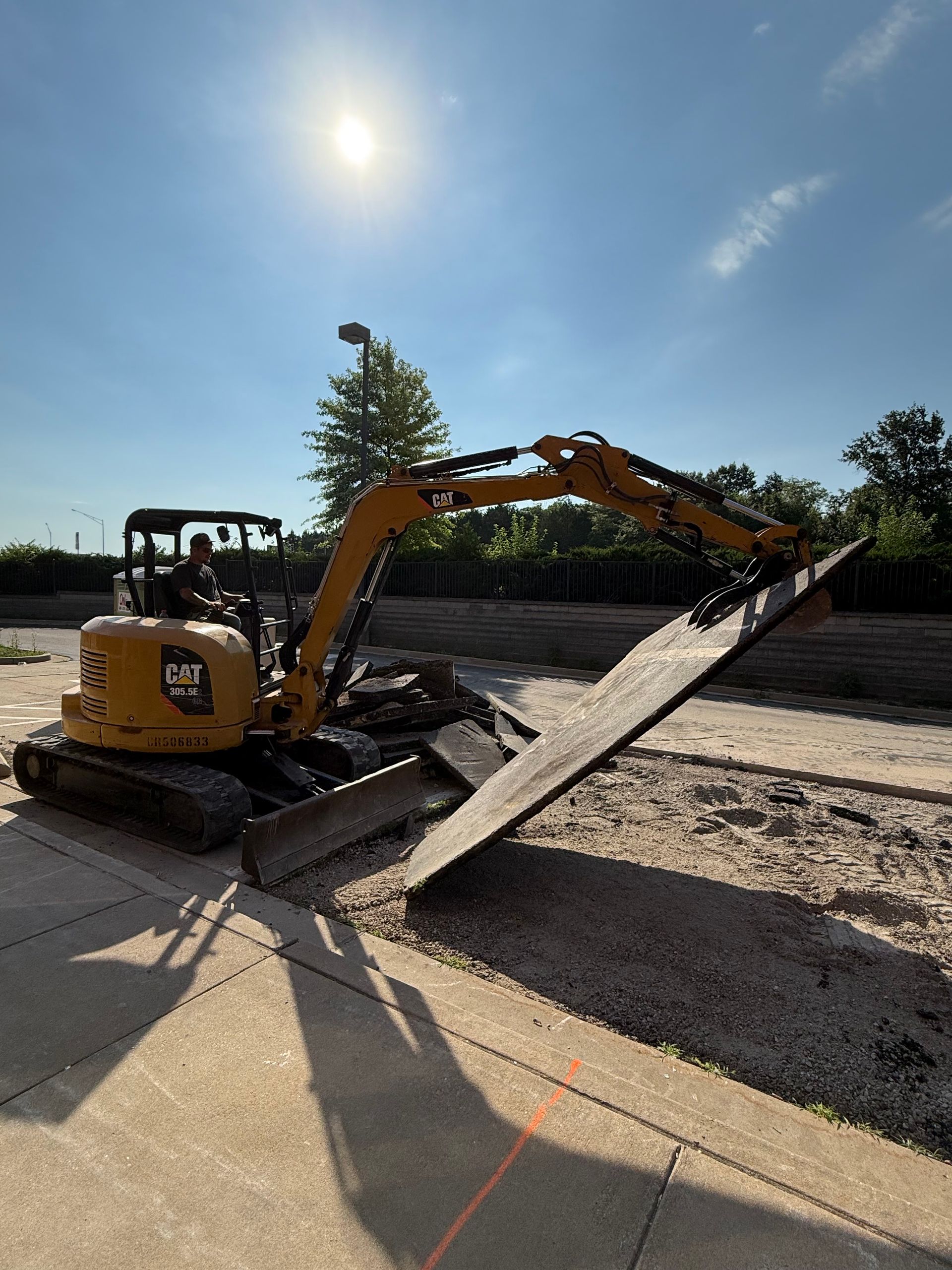 Yellow excavator loading a large metal ramp on a sunny construction site.