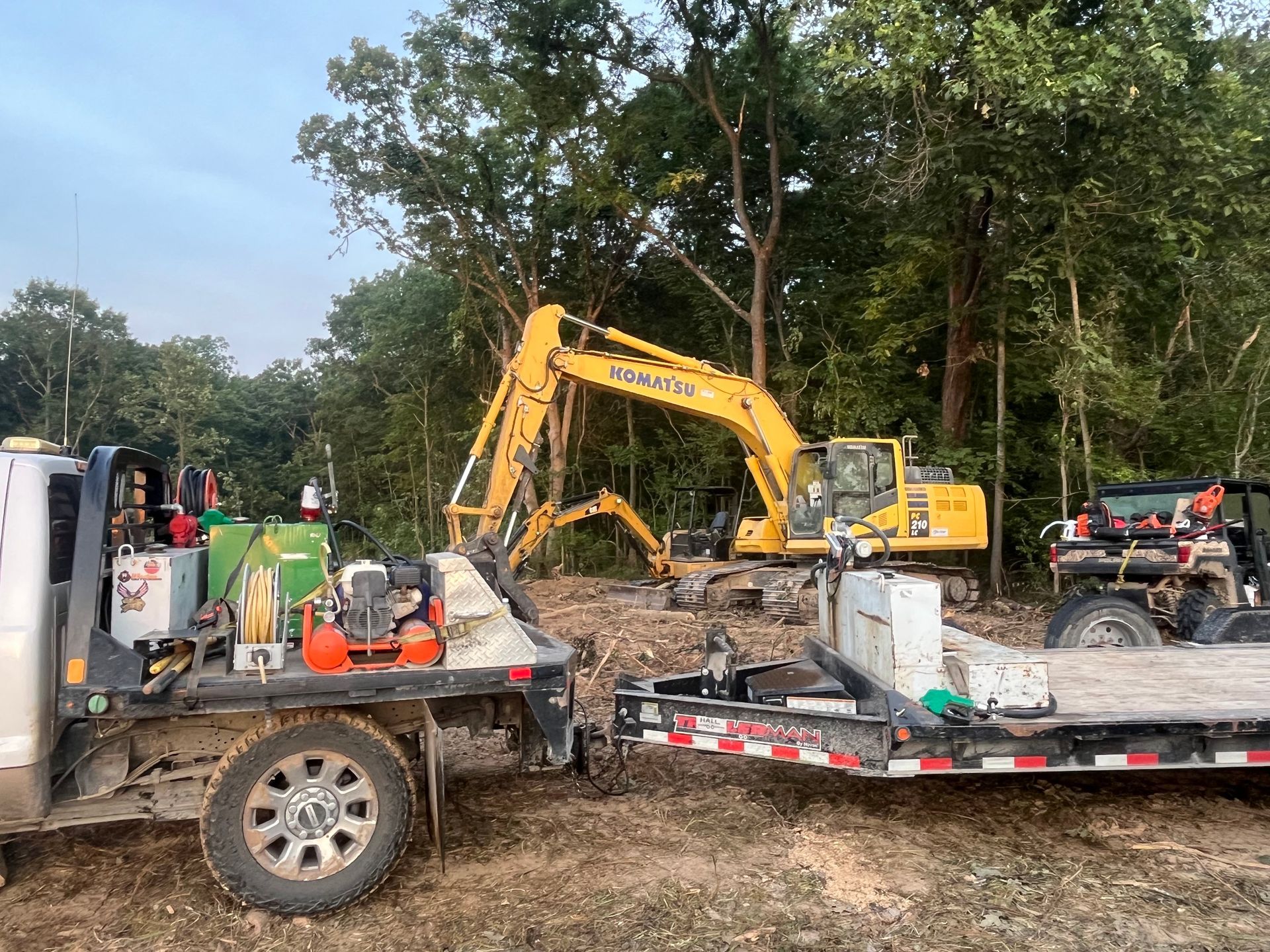 Yellow excavator at a construction site beside trailers and equipment in a wooded area