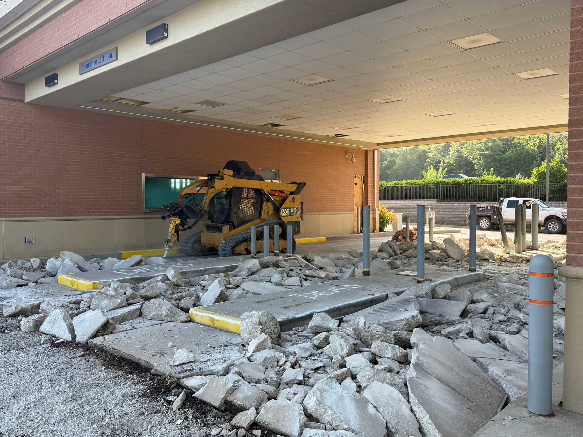 Demolition debris outside a building entrance, with a yellow excavator under the overhang