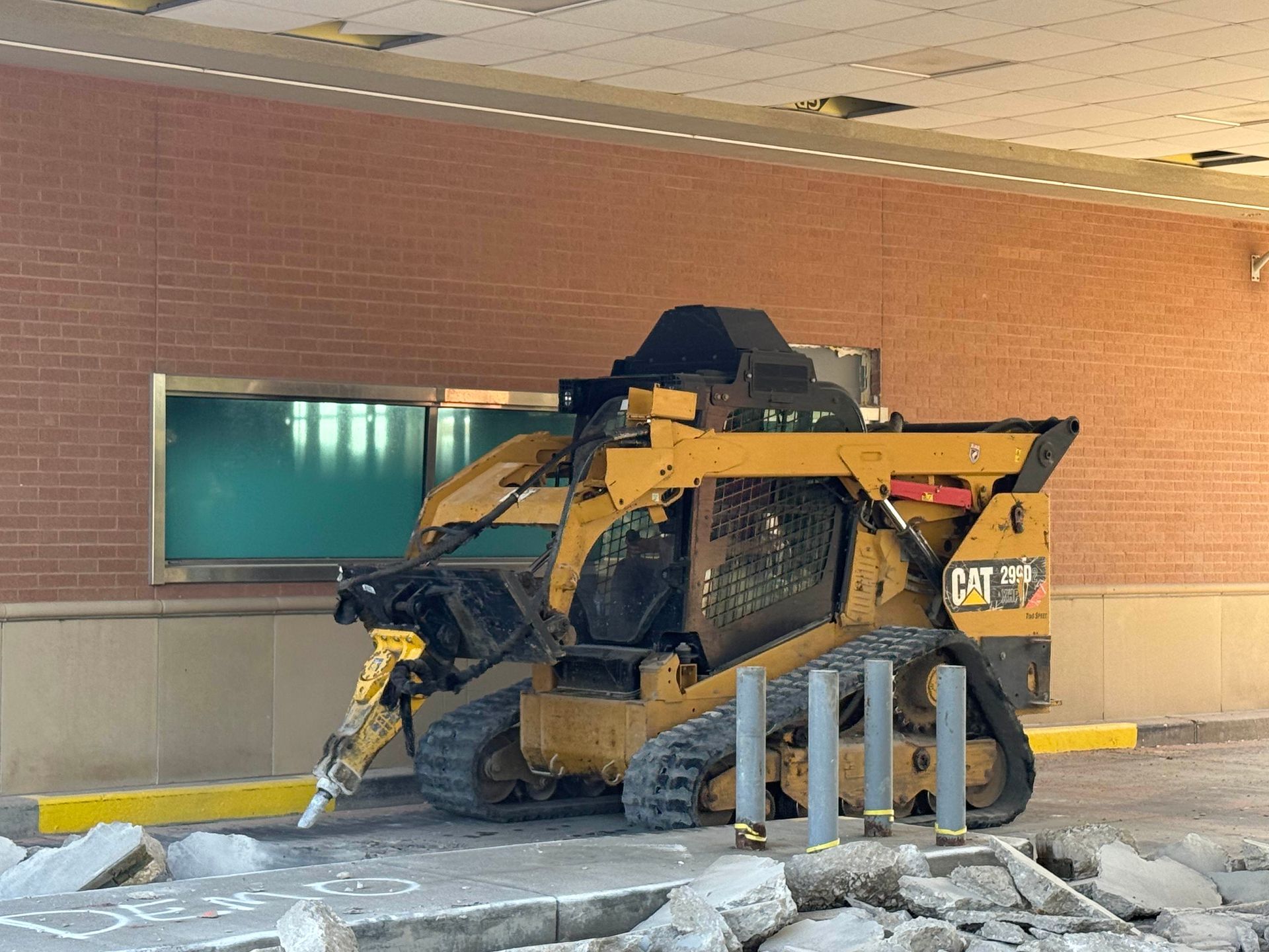 Yellow skid-steer loader crushed against a brick wall outside a building, with broken debris on the ground
