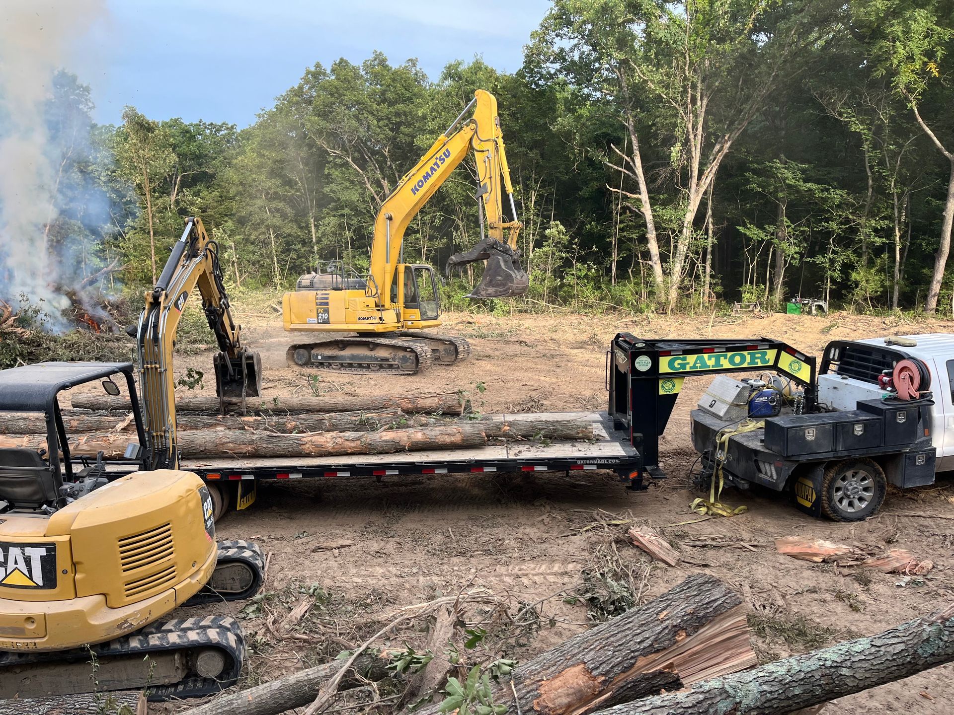 Two excavators and an off-road vehicle at a muddy construction site with trees in the background