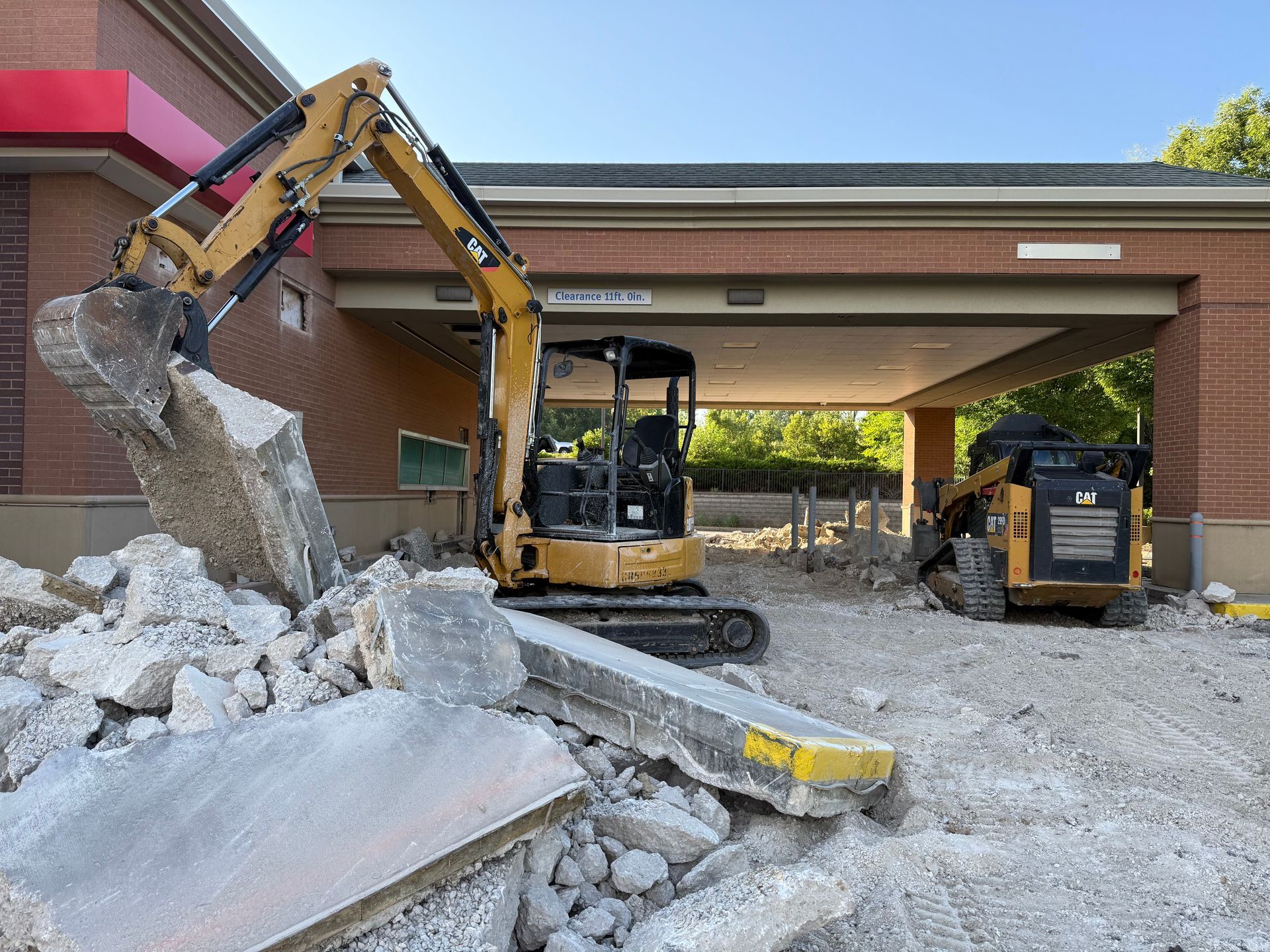 Construction machinery clearing rubble at a building entrance under a covered walkway