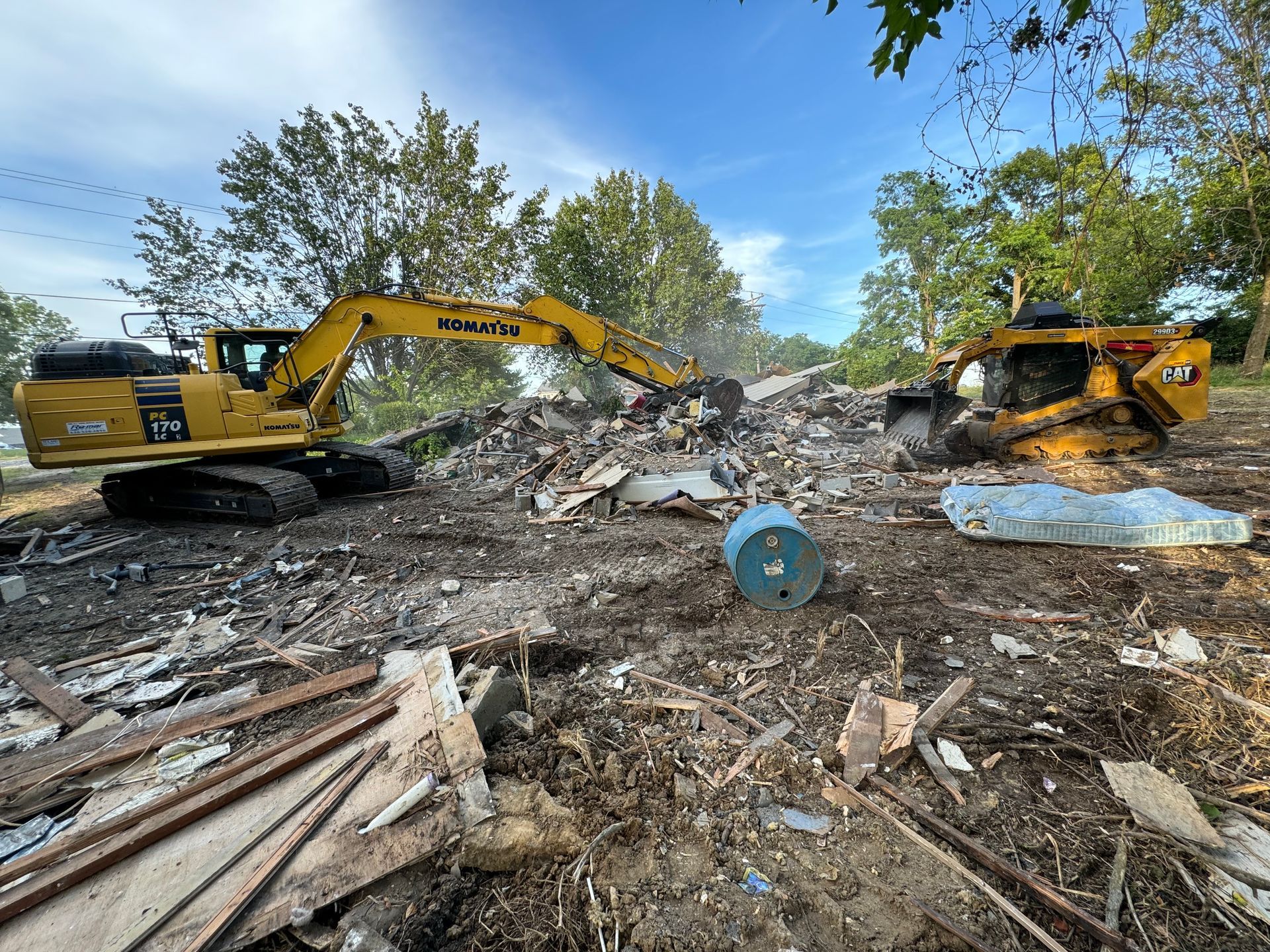 Two yellow excavators clearing a rubble-strewn demolition site under a blue sky.