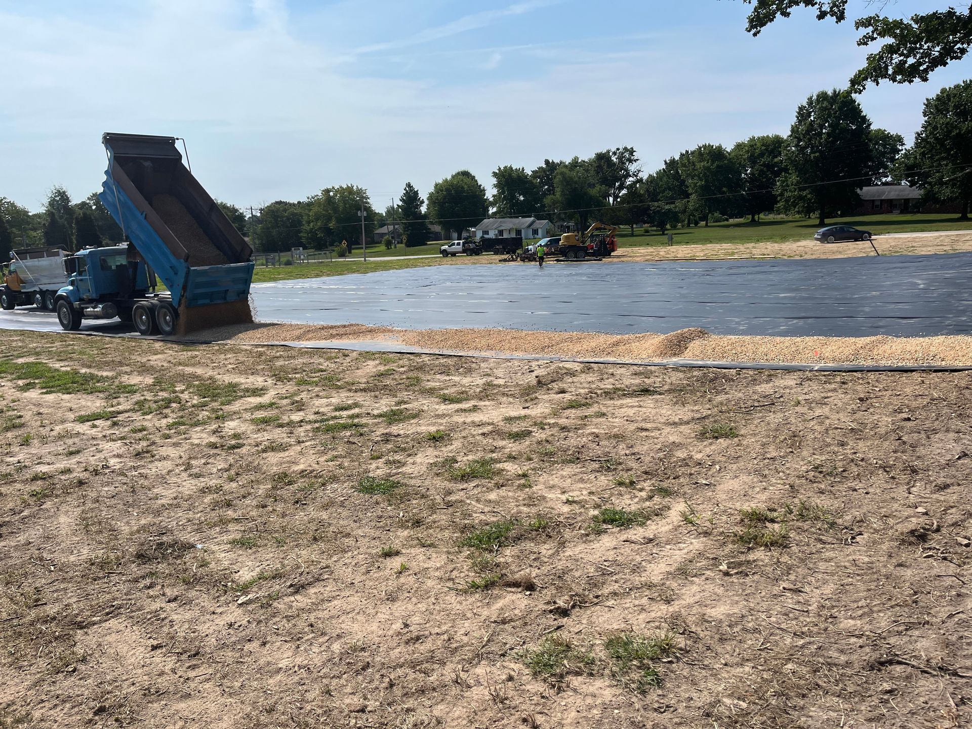 Dump truck unloading dirt near a muddy riverside under a bright blue sky