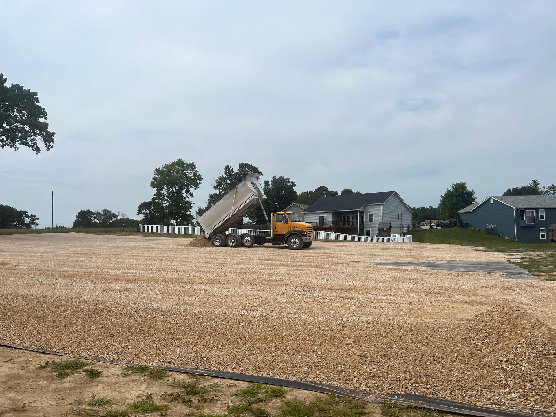 Dump truck unloading gravel at a construction site under a cloudy sky