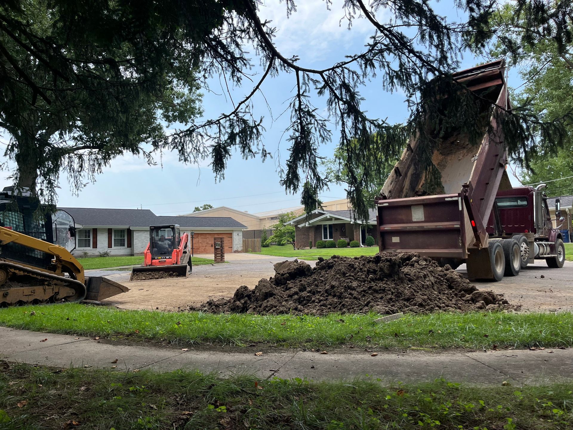 Construction equipment moving dirt in a yard with houses in the background