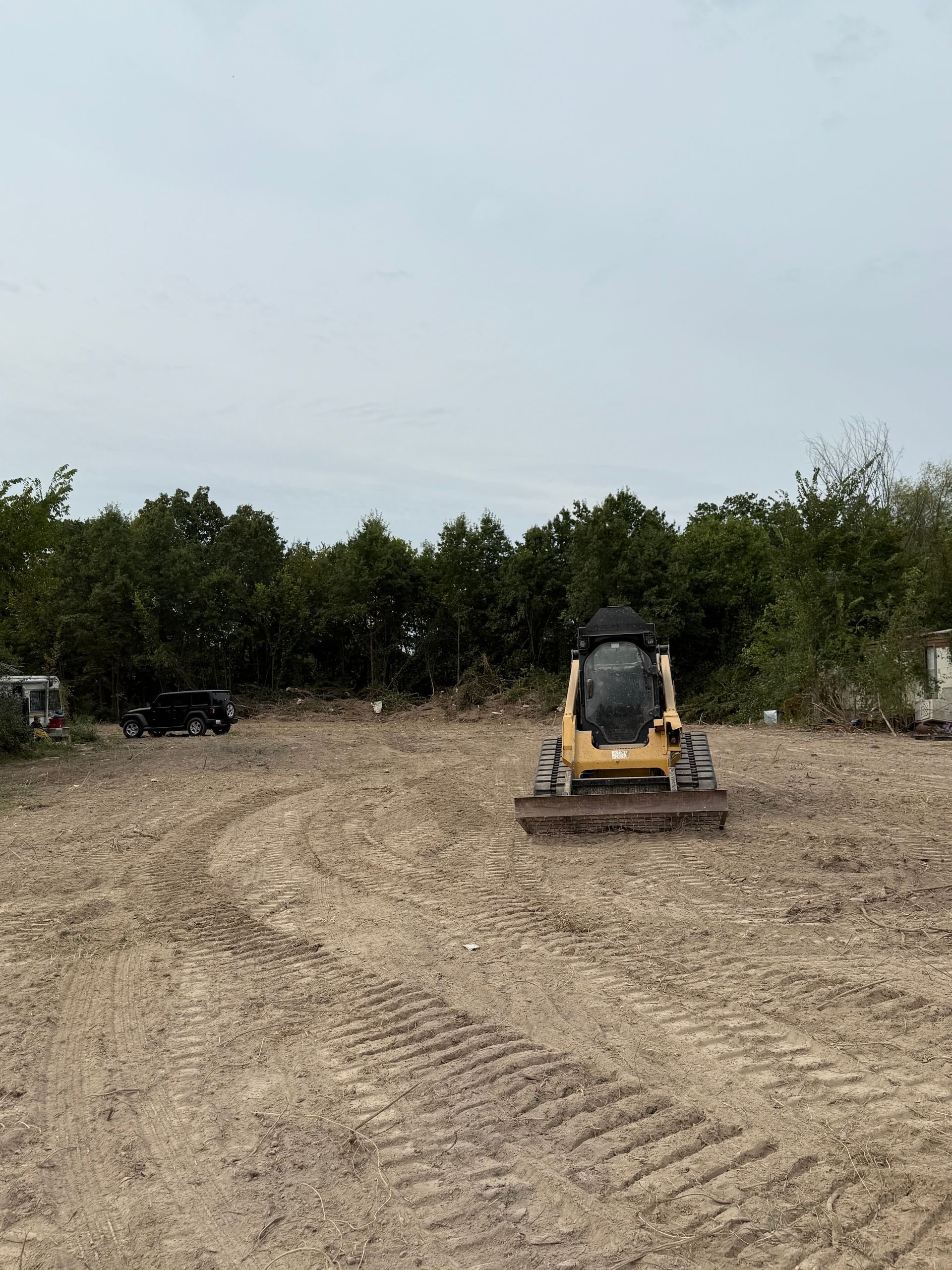 Yellow excavator on a dirt lot with trees in the background.