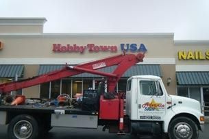 Tow truck with red crane parked in front of HobbyTown USA and a nail salon