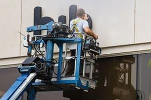 Worker on a blue lift inspecting a building facade near a window opening