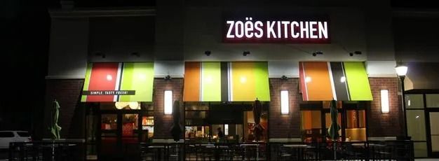 Zoe’s Kitchen storefront at night with colorful illuminated panels and lit windows