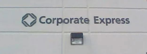 Corporate Express sign on a light wall with a small black square fixture below it
