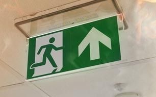 Green emergency exit sign with running figure and upward arrow, mounted on ceiling