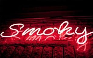 White neon sign spelling “Smoky” glowing over a red background