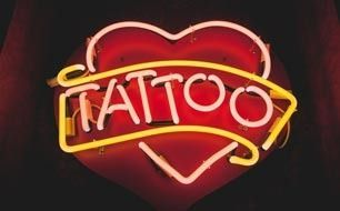 Neon tattoo sign glowing in red and yellow on a dark background