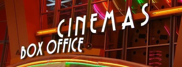 Neon “CINEMAS” and “BOX OFFICE” signs glowing on a theater exterior at night