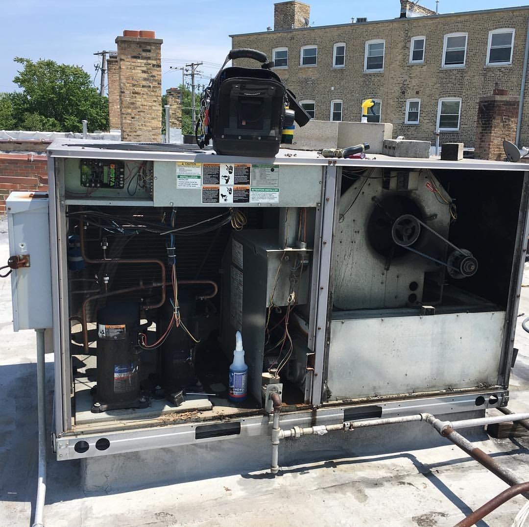 HVAC unit on a rooftop with open panels, showing internal components. A toolbox sits on top.