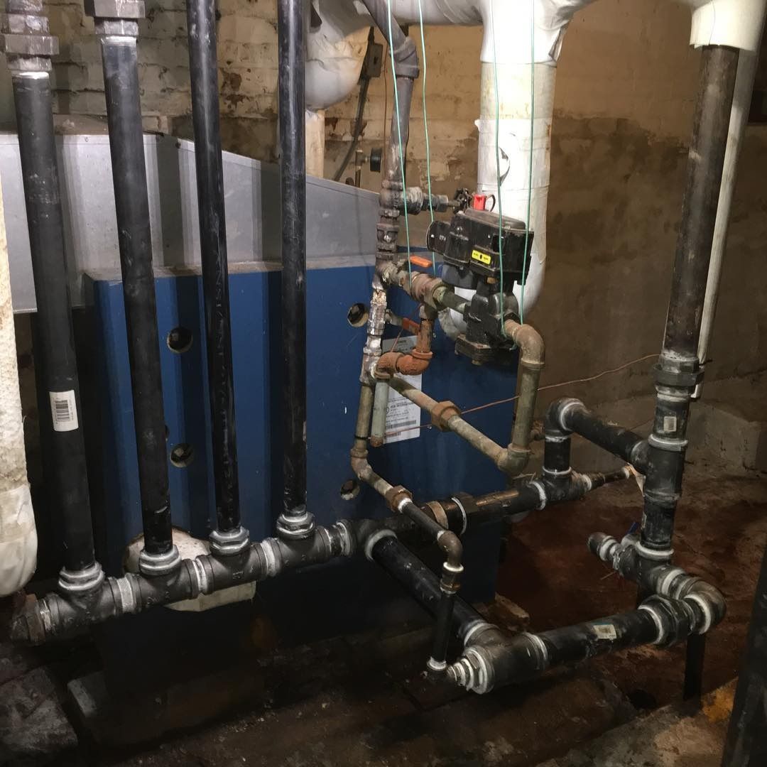 Plumbing system with black pipes connected to a blue water tank in a basement setting.