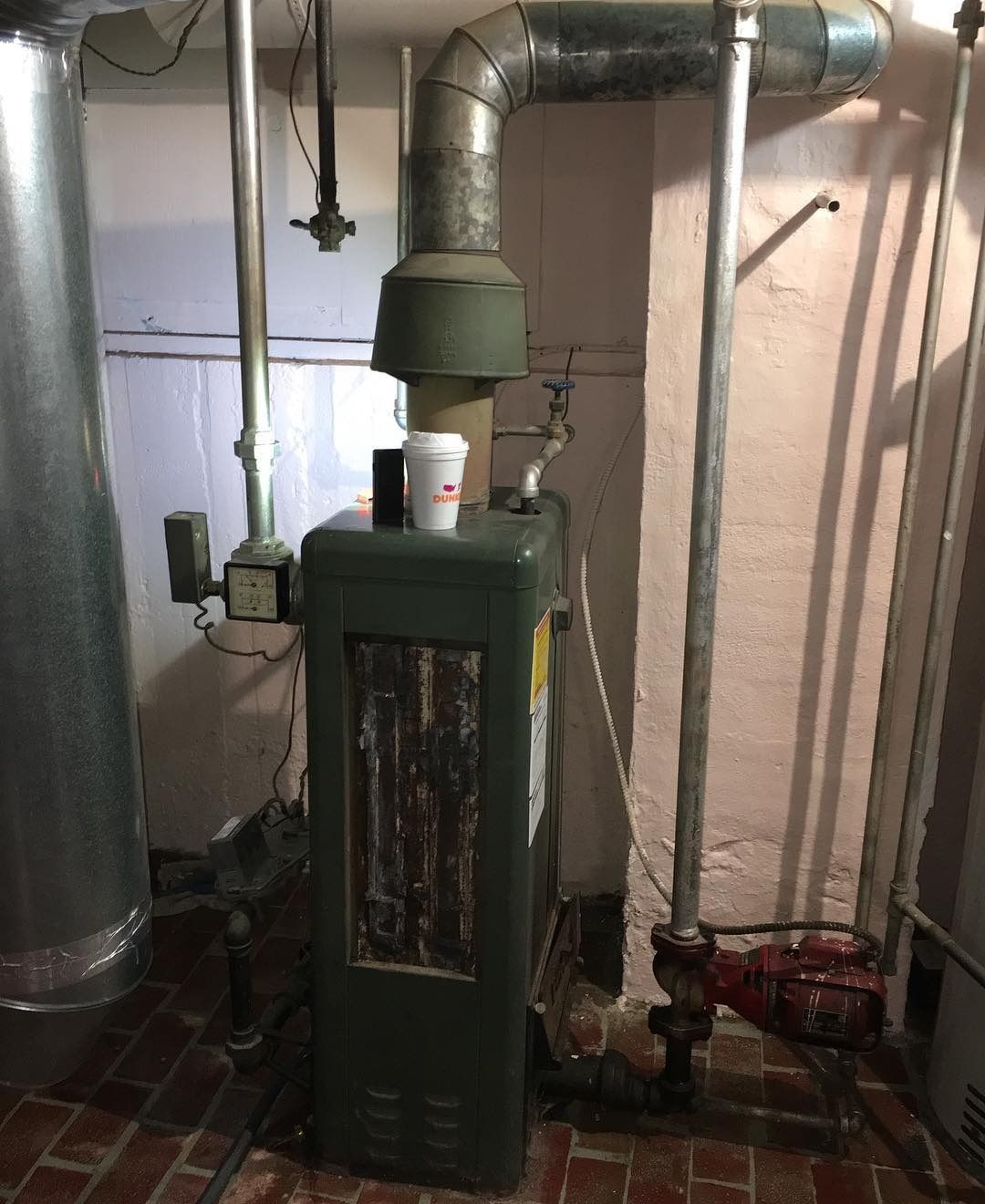 A furnace in a basement with silver pipes and a red pump.