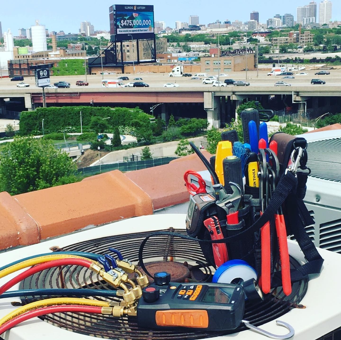 HVAC tools on rooftop unit; city skyline in background.