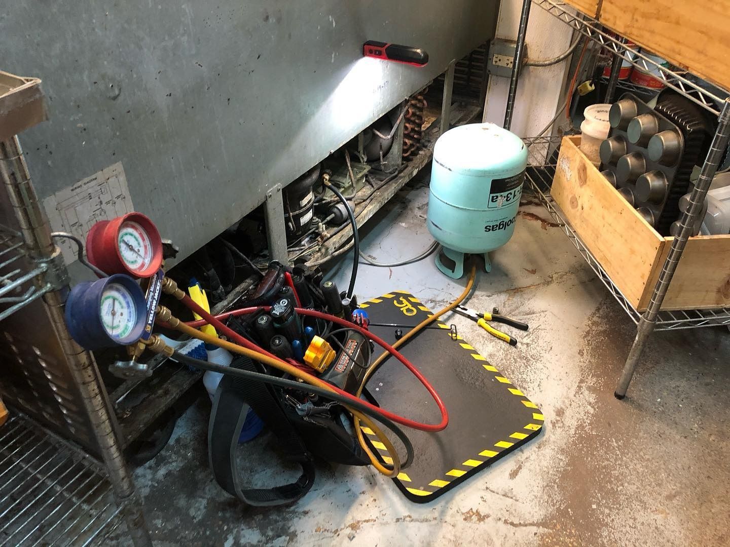 Refrigerator repair with gauges, refrigerant tank, and tools in a commercial kitchen.