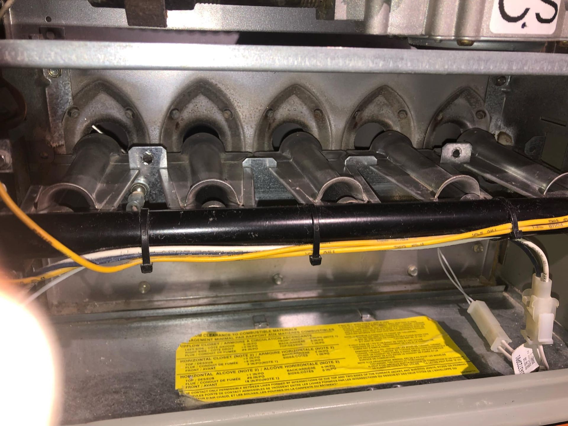 Interior of a furnace with burner tubes, wiring, and a yellow warning label.