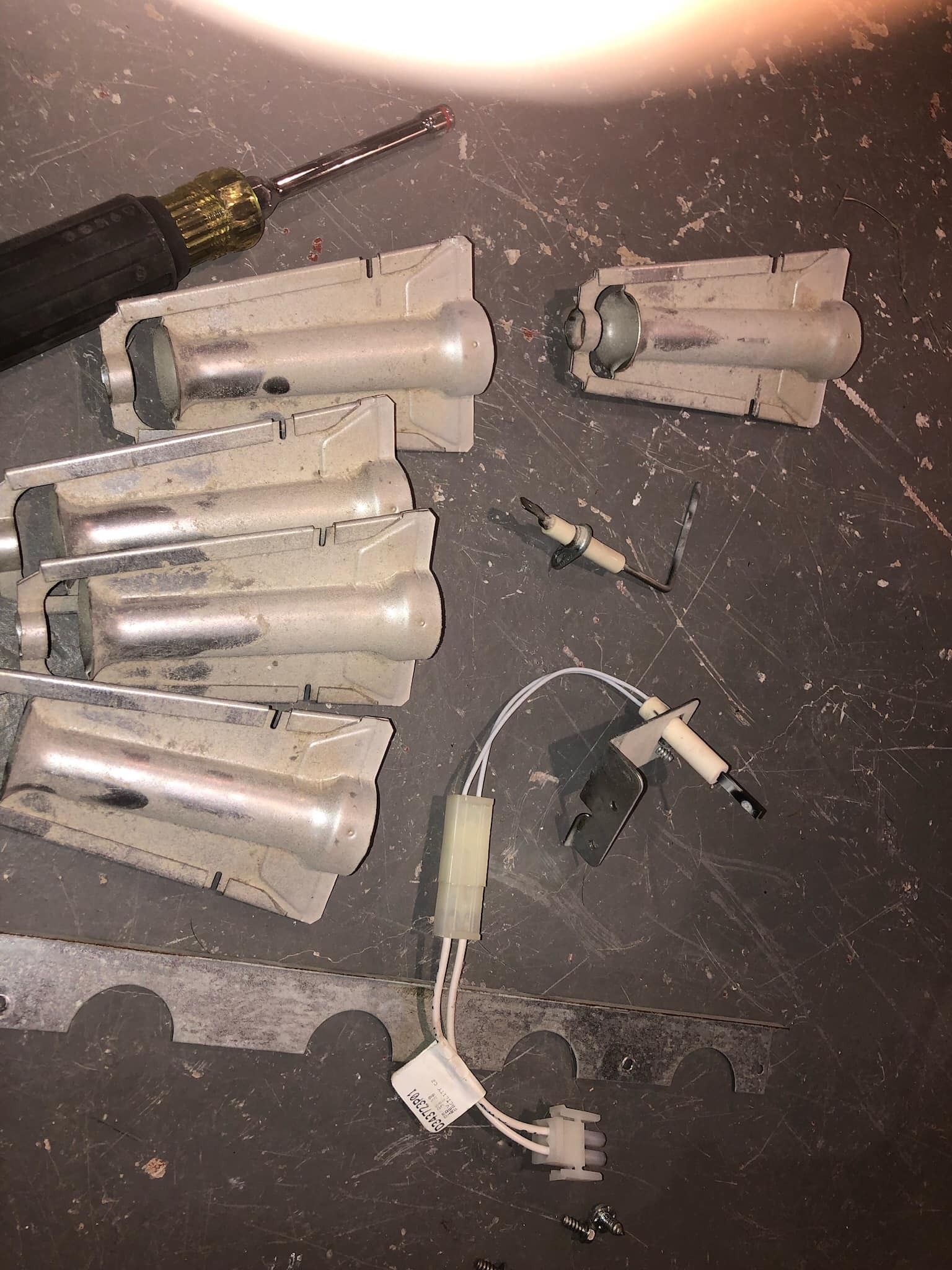 Various disassembled fluorescent light components scattered on a dark surface, with a screwdriver.