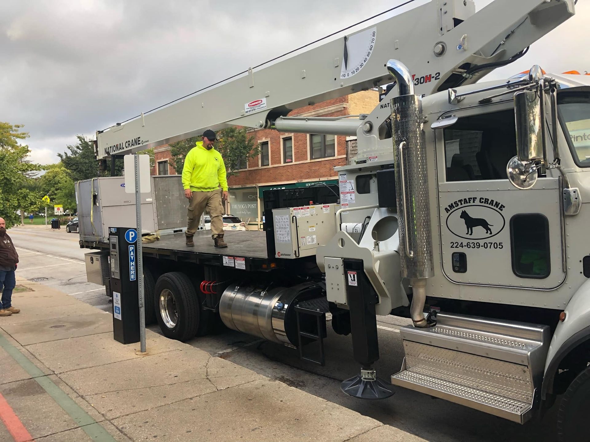 Person on a crane truck; wearing a neon vest. Truck parked on a city street.