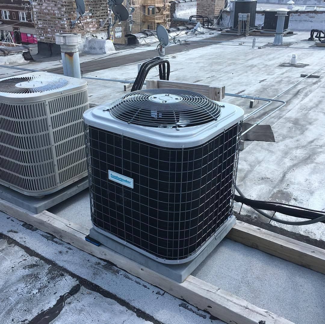 Two rooftop HVAC units on a snow-covered flat surface; the one in focus has a fan on top.