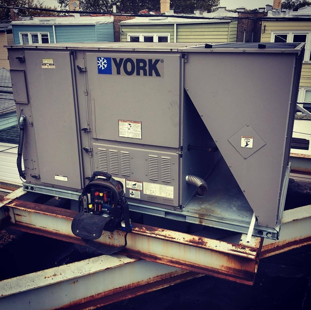 York HVAC unit on a rooftop. Gray metal box, blue logo, and rusted beams.
