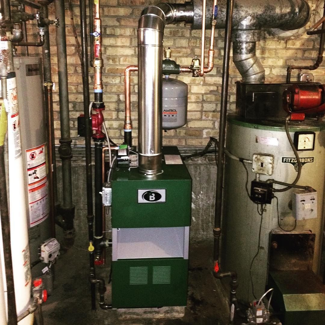A green furnace with a metal chimney and other mechanical equipment in a basement.