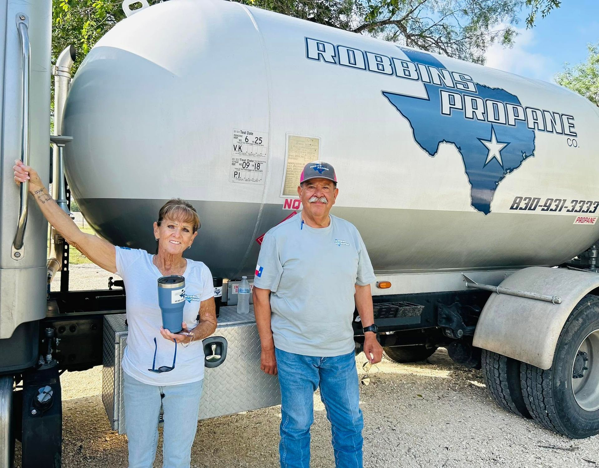 Two people standing beside a silver tanker truck painted with Texas and 