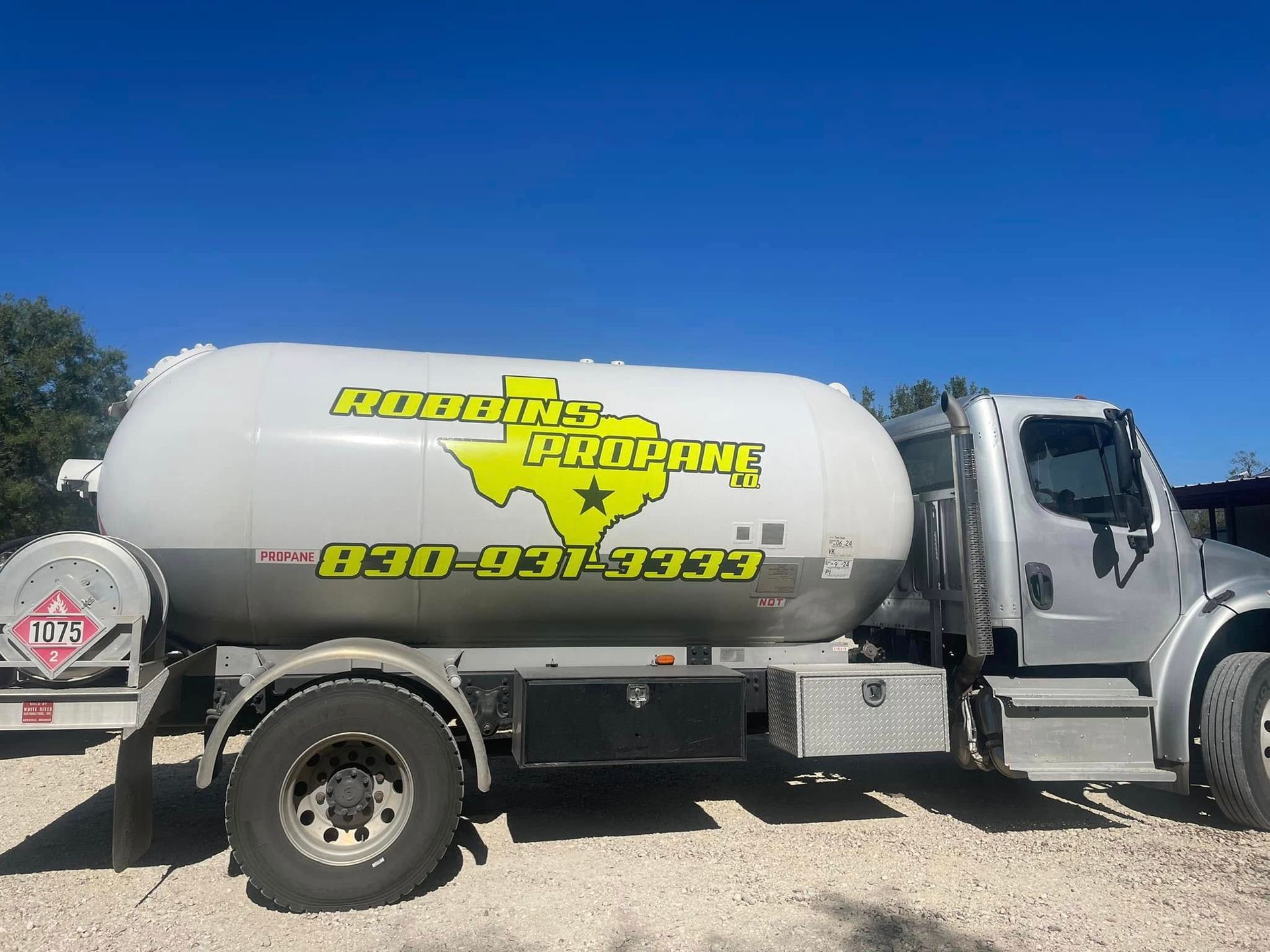 Silver water tanker truck with bright yellow company logo parked on a dirt lot under a clear blue sky