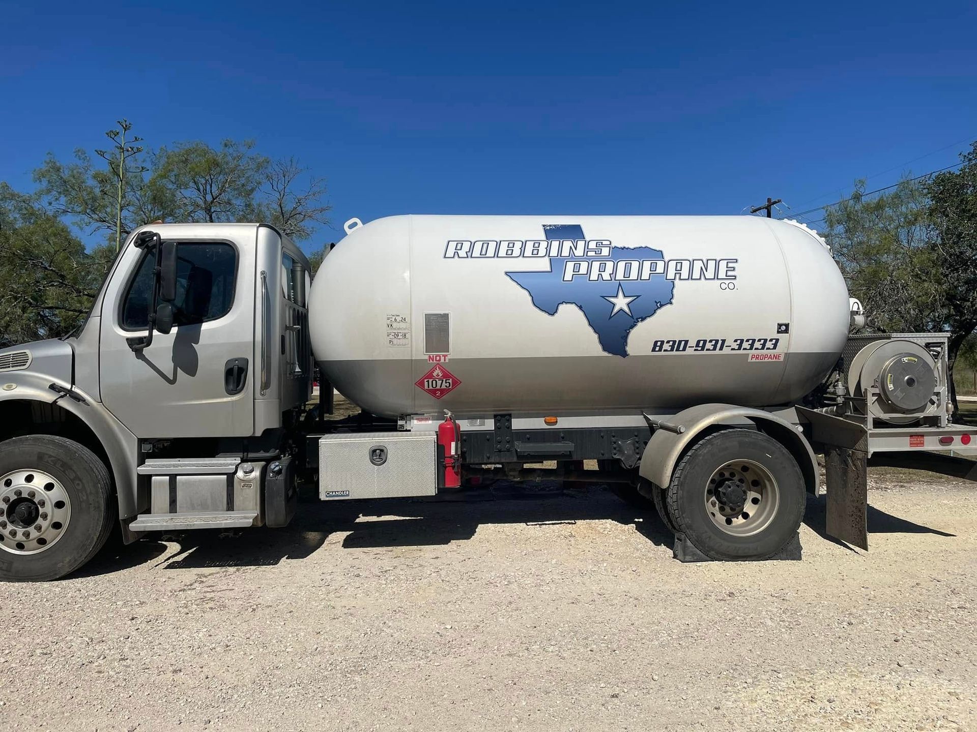 White fuel tanker truck parked on gravel under a clear blue sky